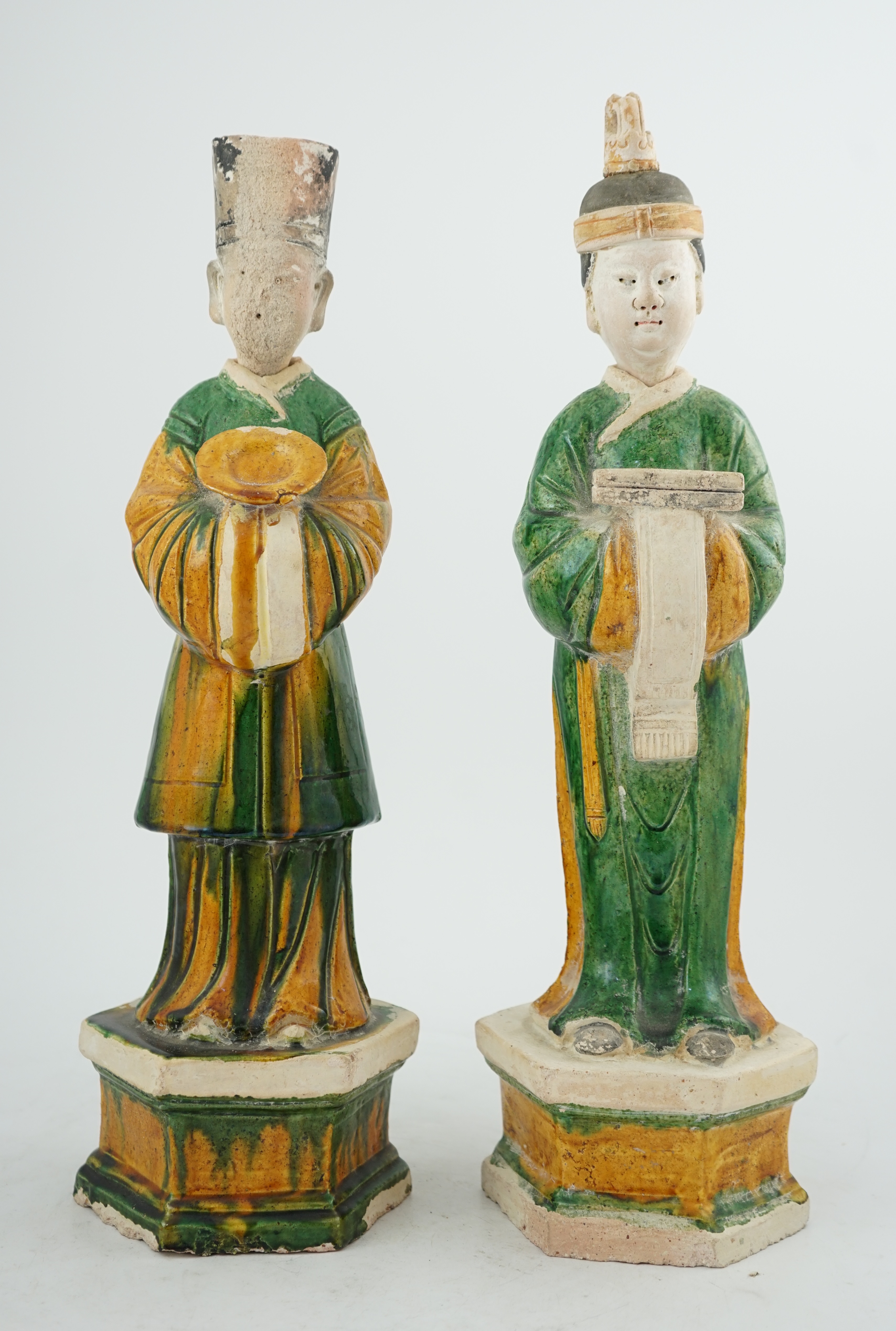 Two tall Chinese sancai figures of attendants, Ming dynasty, the male figure holding a dish and the female figure a box, each standing on a hexagonal base, largest 47cm high. Condition - some wear to face